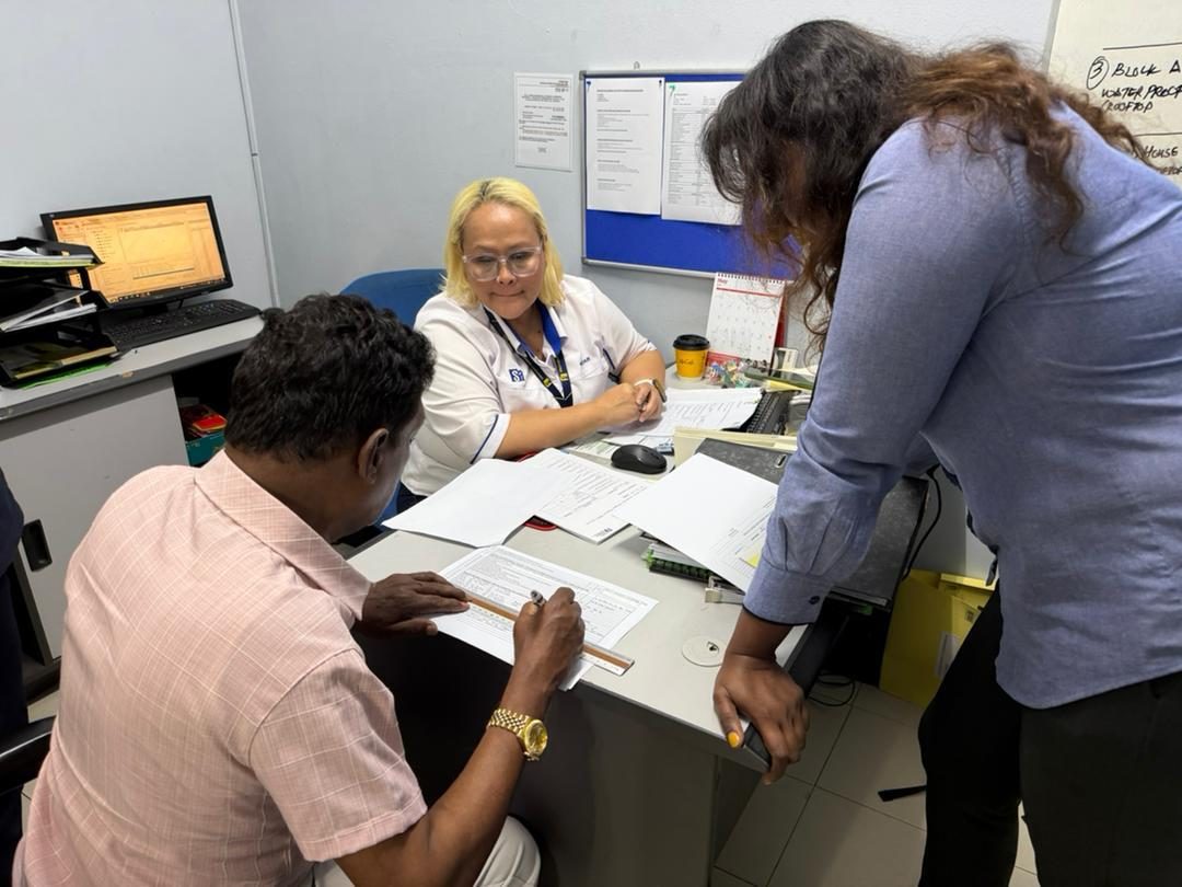 Nelfar Zulkifli going through documents at a management office desk with two colleagues