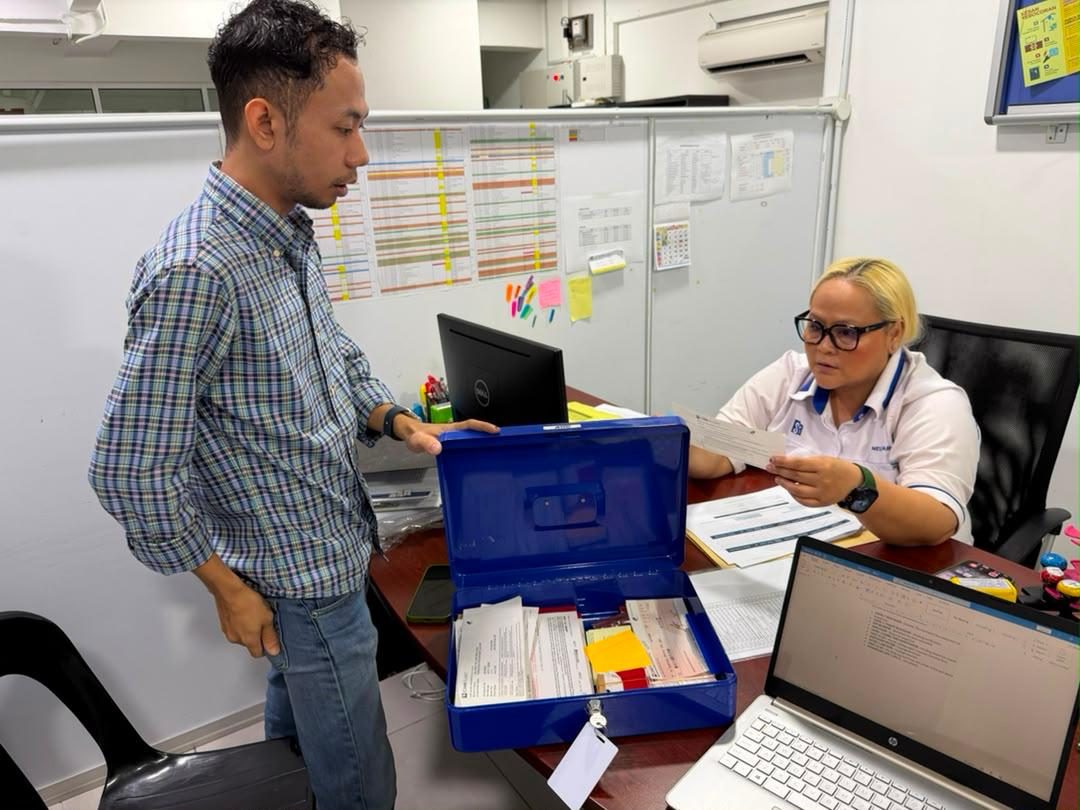 Nelfar Zulkifli at her desk with records and a planning board on the wall behind