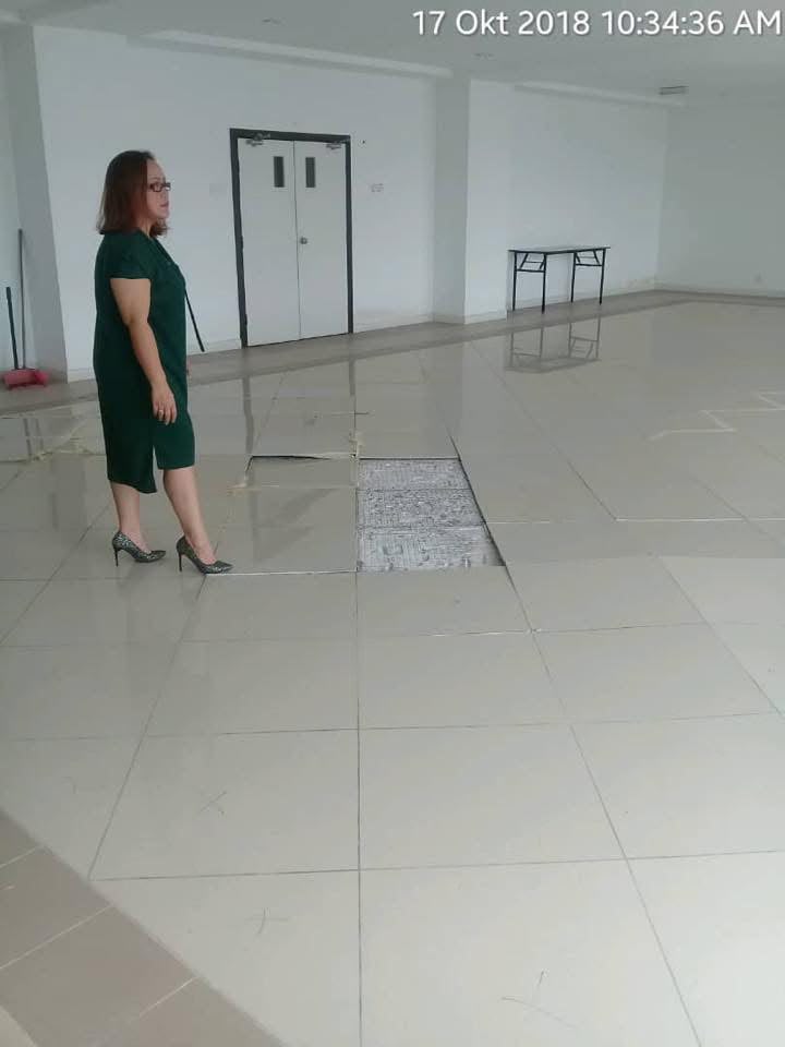 Inspecting a lifted floor tile in an empty function hall