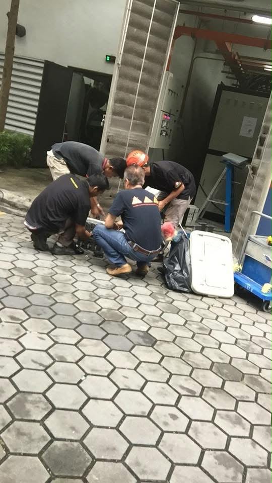 Technicians working on a dismantled pump component on the pavement outside an electrical switch room