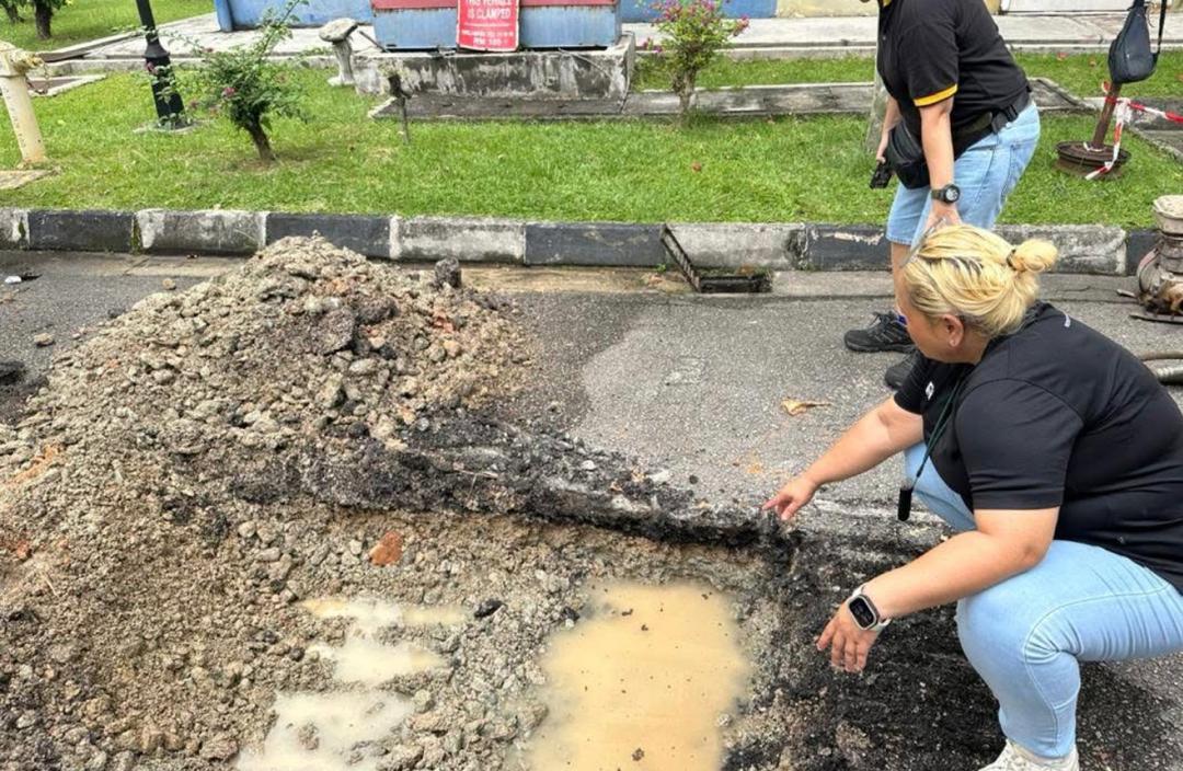 Nelfar Zulkifli crouched at an excavated section of road, pointing into a water-filled trench