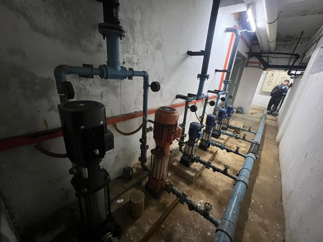 A vertical multistage booster pump set and pipework in a basement plant room