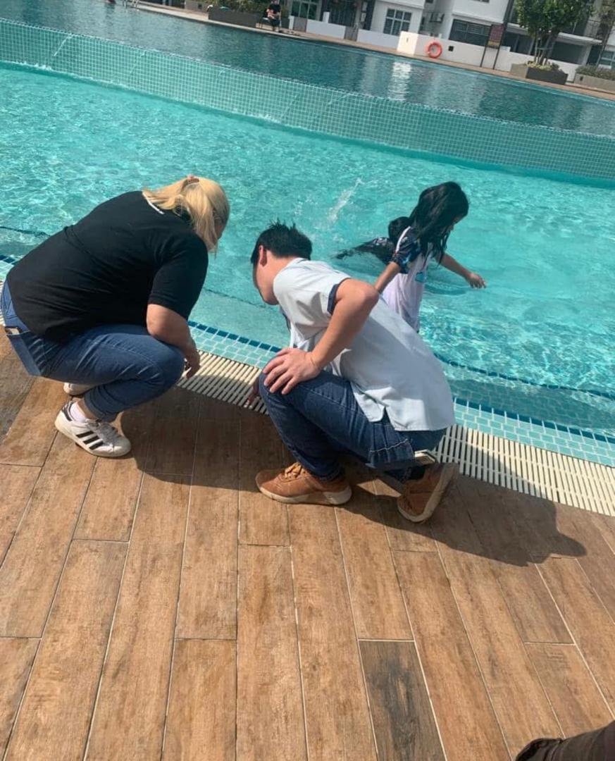 Three people crouched at the edge of a swimming pool, inspecting the coping and the overflow channel