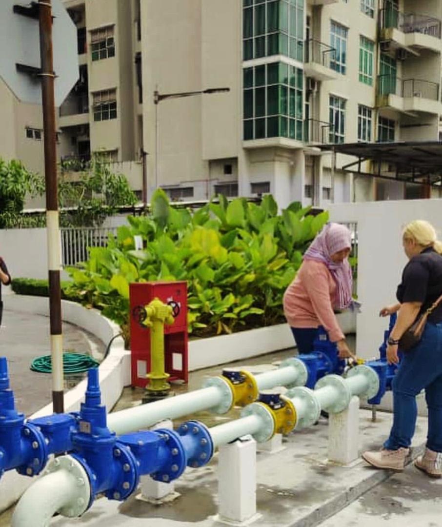 Nelfar Zulkifli and a colleague at a run of bulk water meters and valves outside a condominium