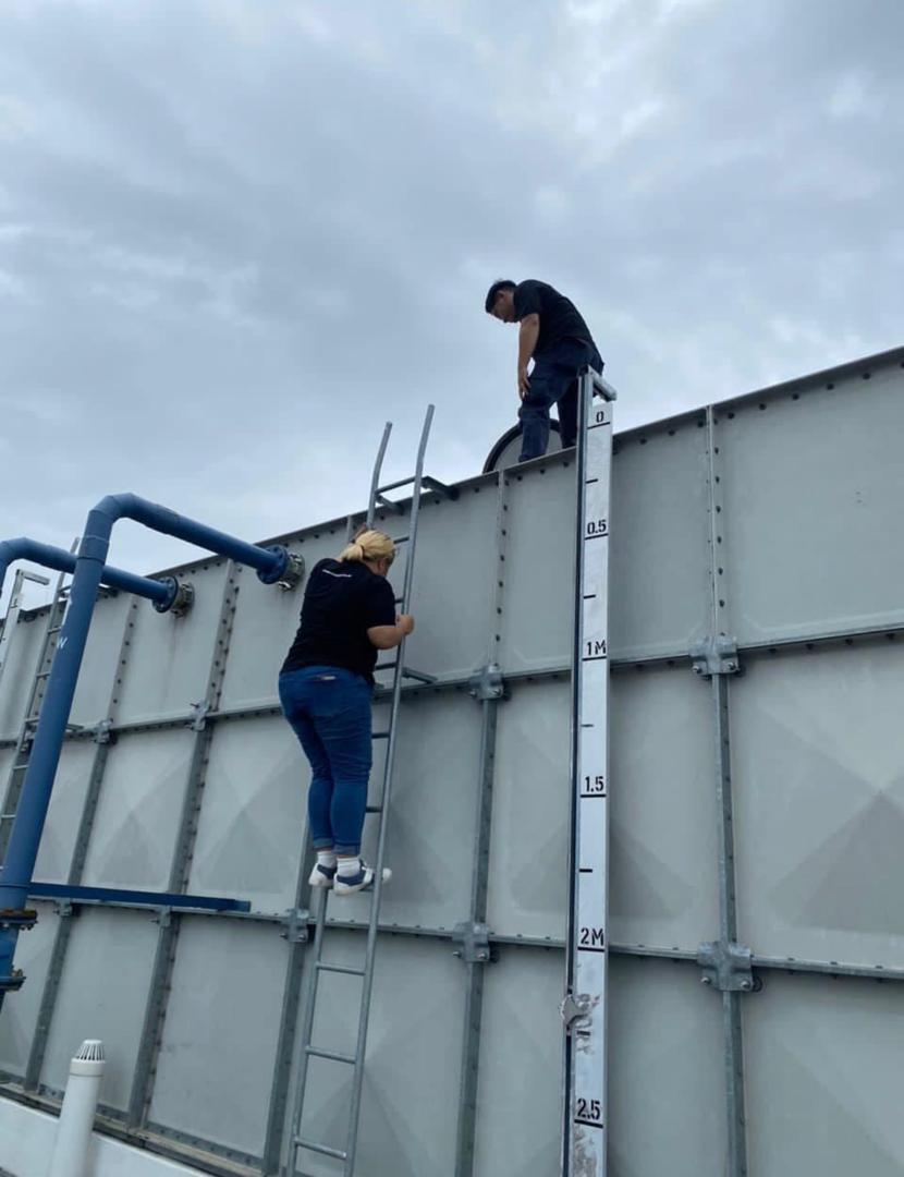 Climbing a ladder to the top of a sectional panel water tank, with a colleague already on the tank roof